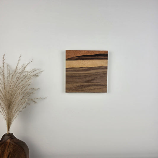 Wooden wall art piece on a plain wall with decorative elements below. Jennifer Mourato Art Collection