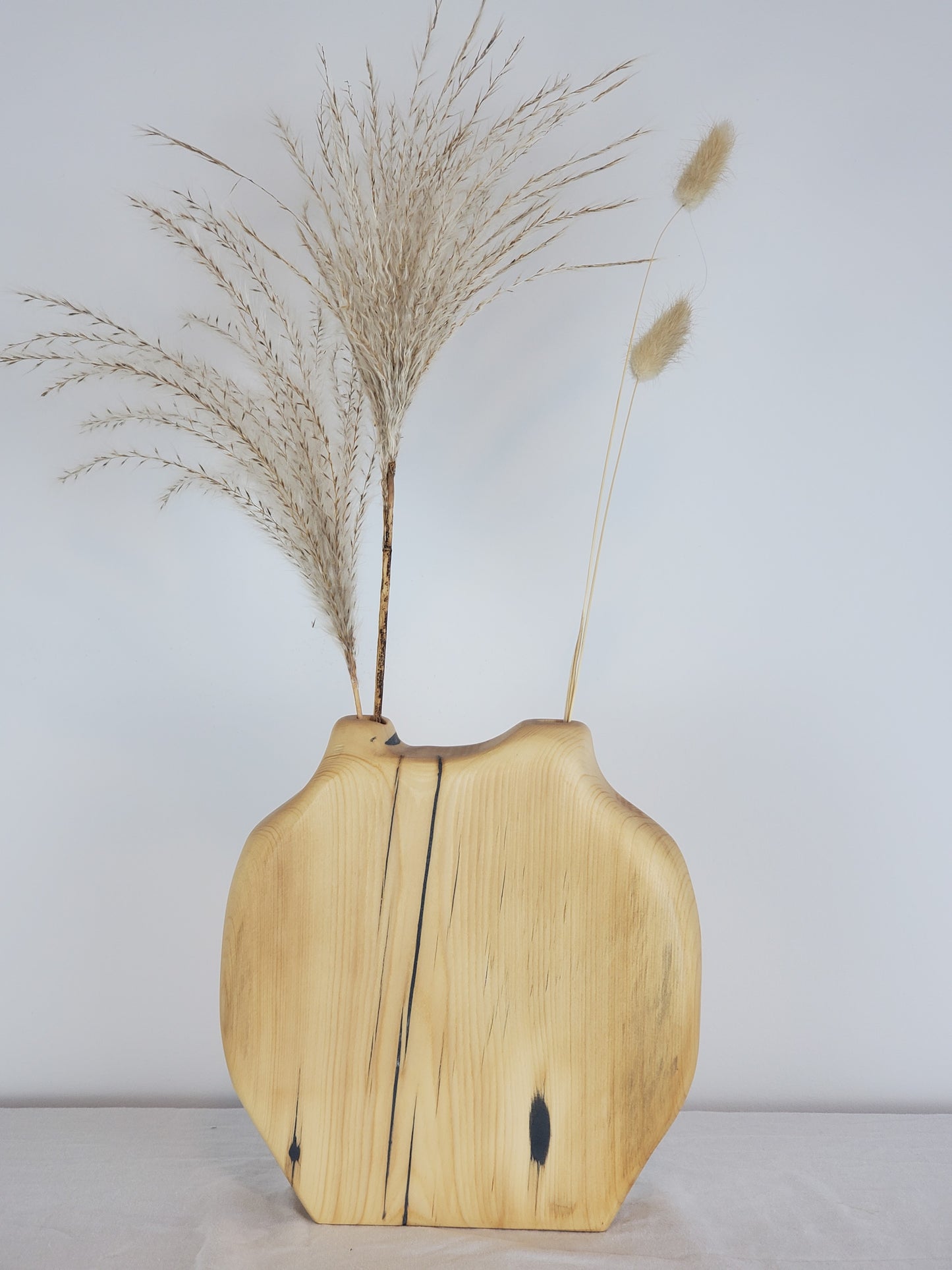 Wooden vase with natural finish holding dried plants against a plain background