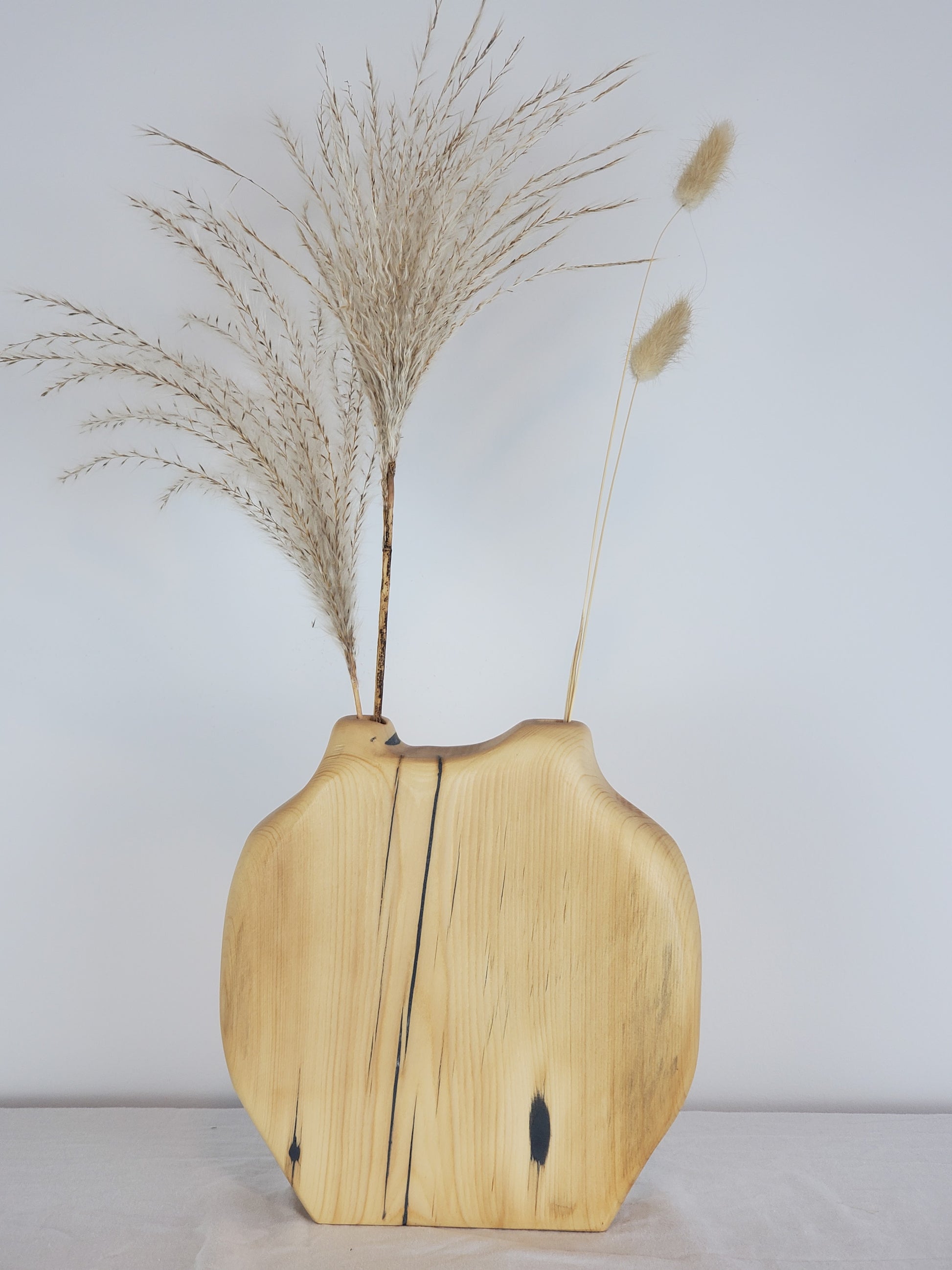 Wooden vase with natural finish holding dried plants against a plain background