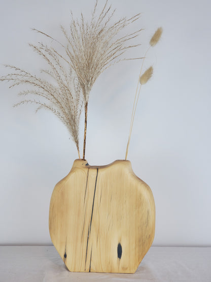 Wooden vase with natural finish holding dried plants against a plain background