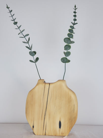 Wooden vase with a natural split design holding eucalyptus branches on a light background