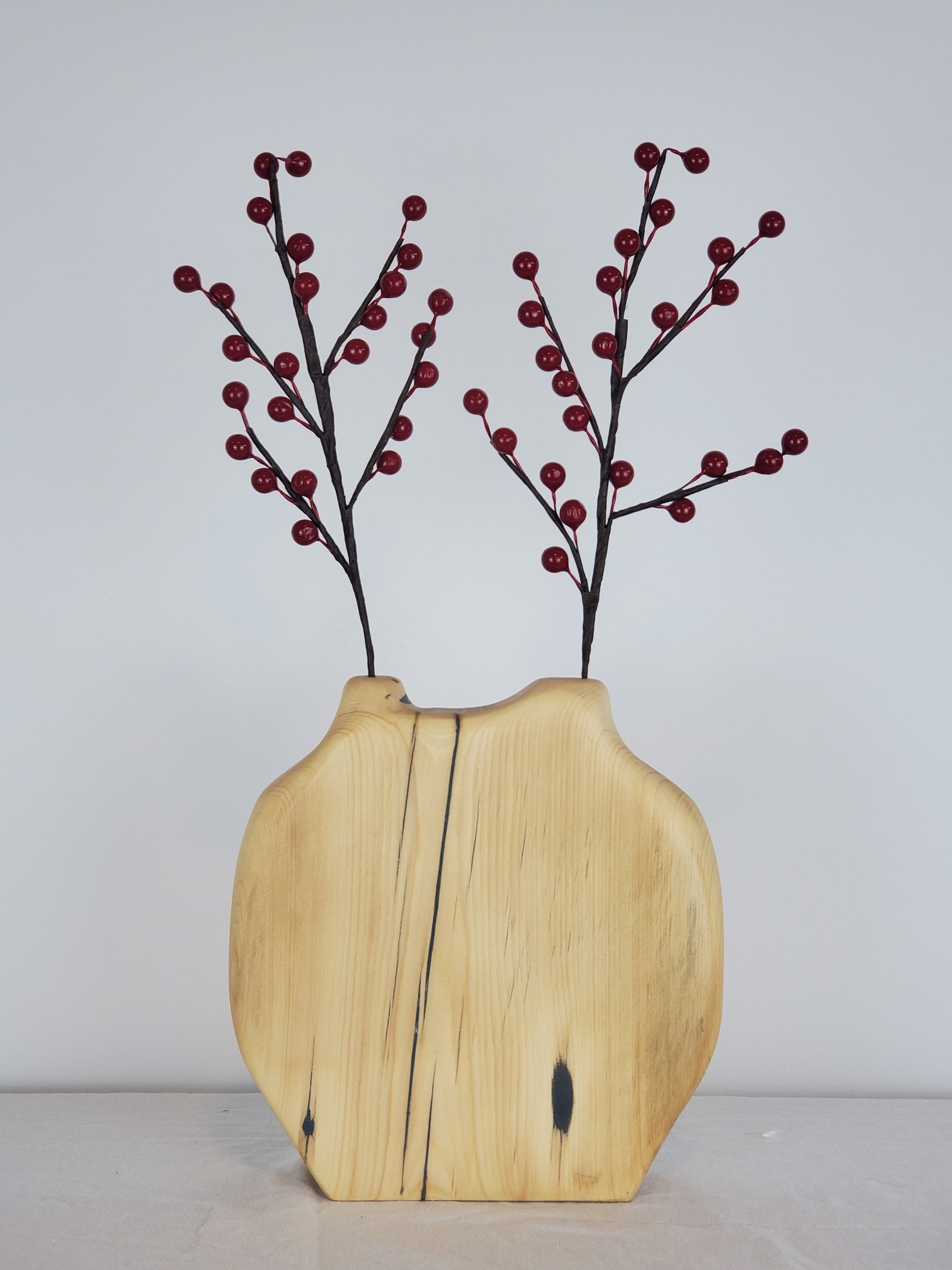 Wooden vase with a natural split design holding red branches against a plain background