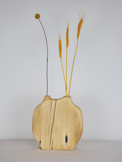 Wooden vase with natural finish holding dried plants against a plain background