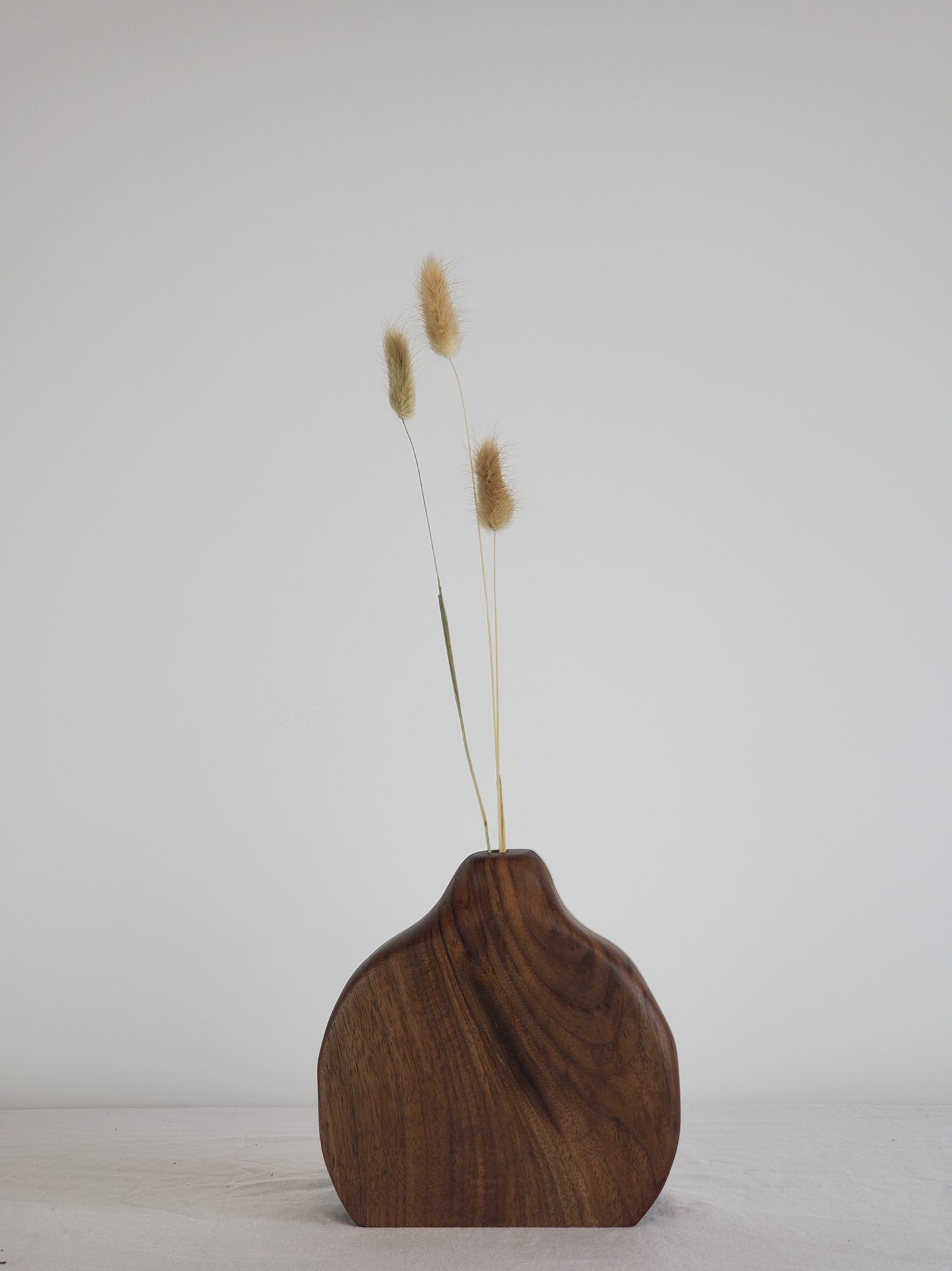 Wooden bud vase with dried grasses on a white wall