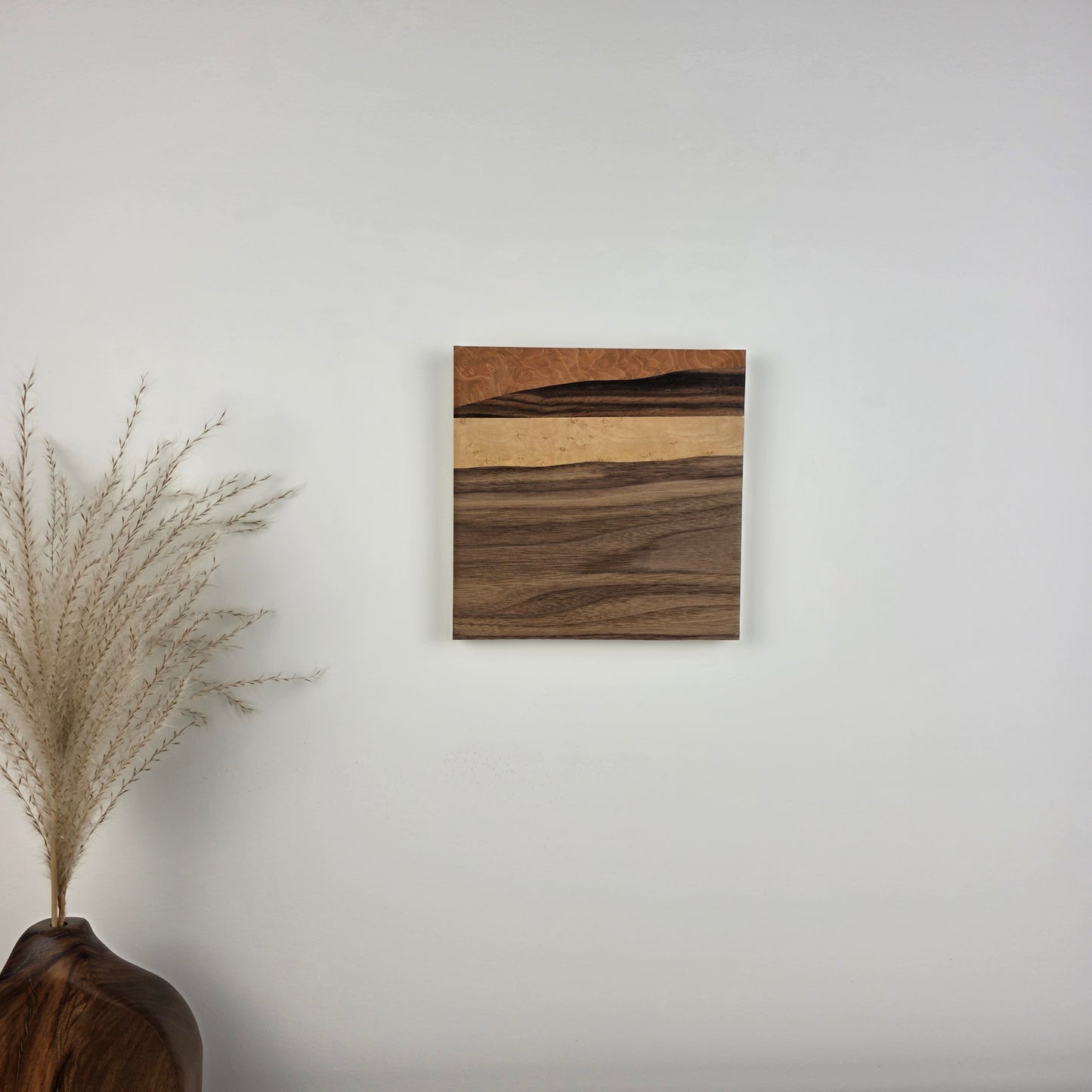Wooden wall art piece on a plain wall with decorative elements below. Jennifer Mourato Art Collection