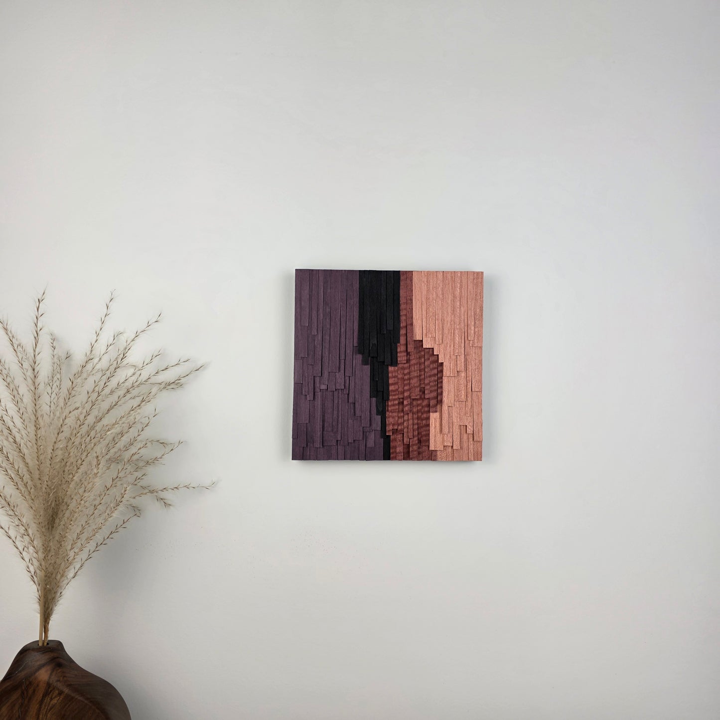 Wooden wall art piece on a white wall with a decorative plant in the corner.