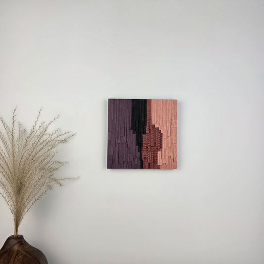 Wooden wall art piece on a white wall with a decorative plant in the corner.