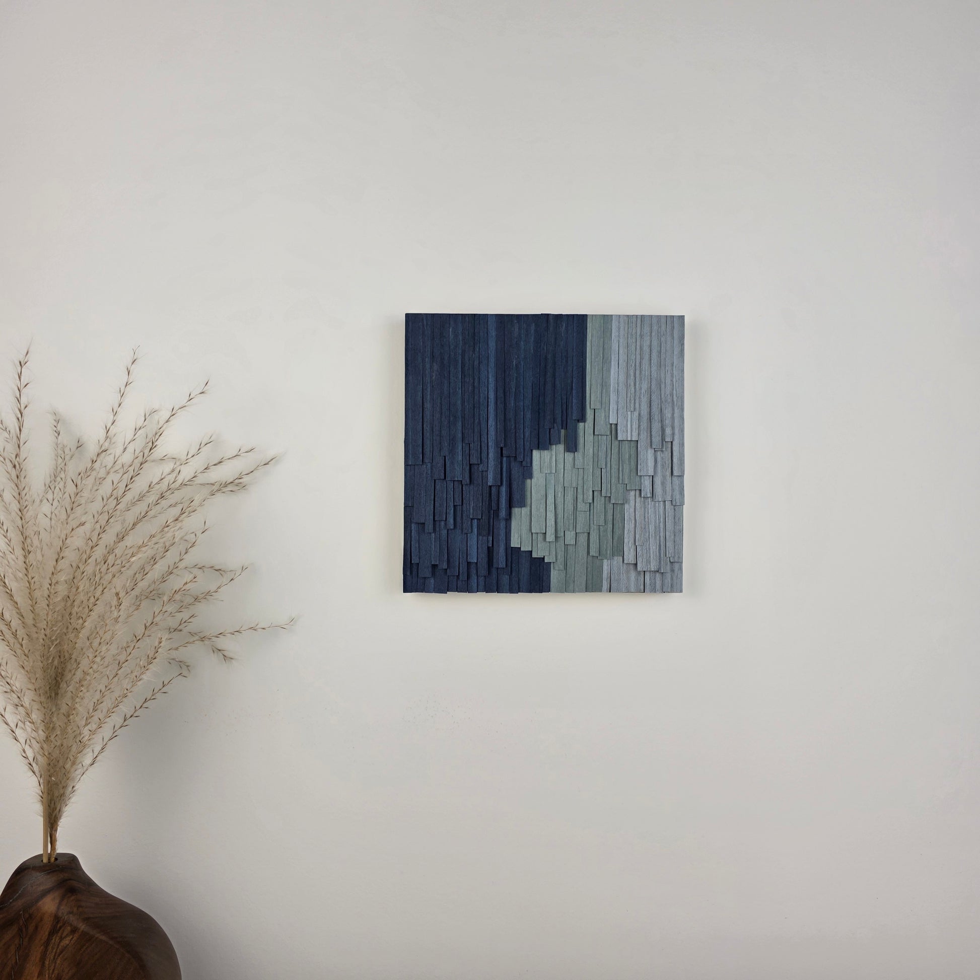 Blue wood ribbon wall art on a white wall above a wood bud vase with dried stem